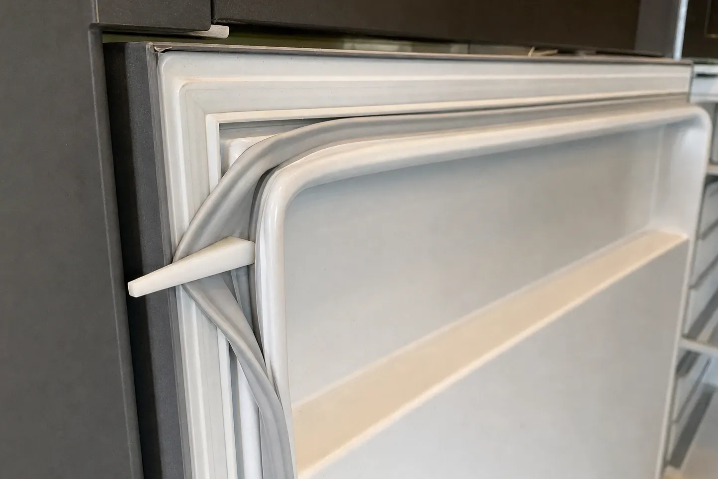 Close-up of a flexible door gasket pulled away from the corner of a refrigerator door liner